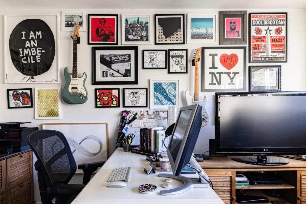 a lot of artwork displayed on wall pc and keyboard placed on working desk