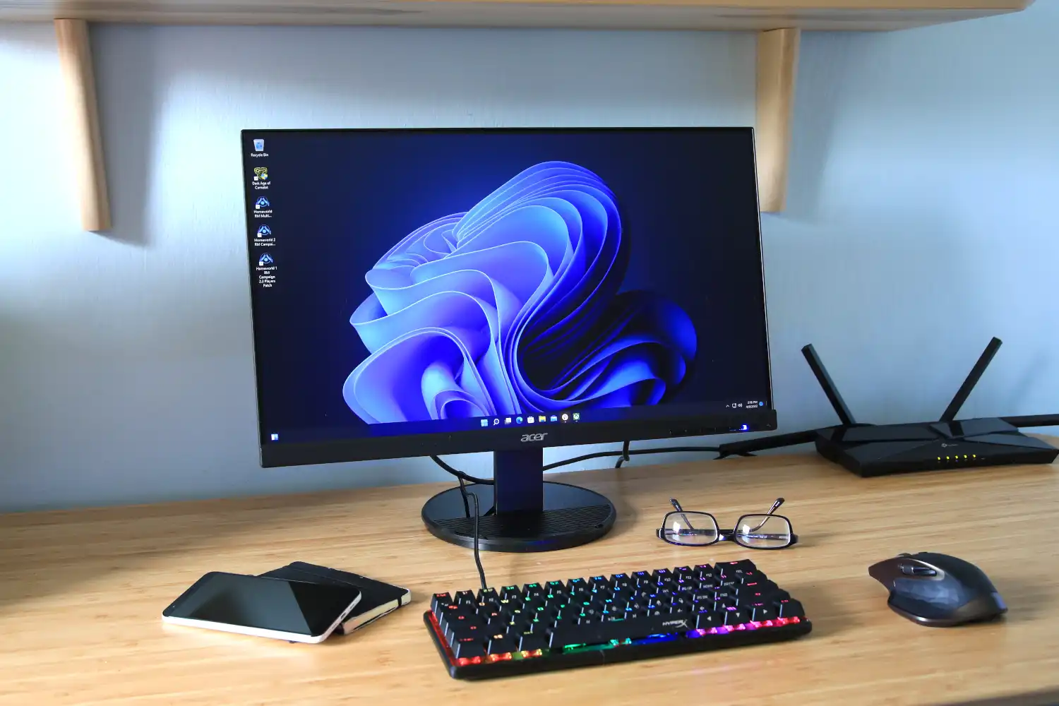 a monitor keyboard glasses internet devicem mobile mouse and notepad placed on a table