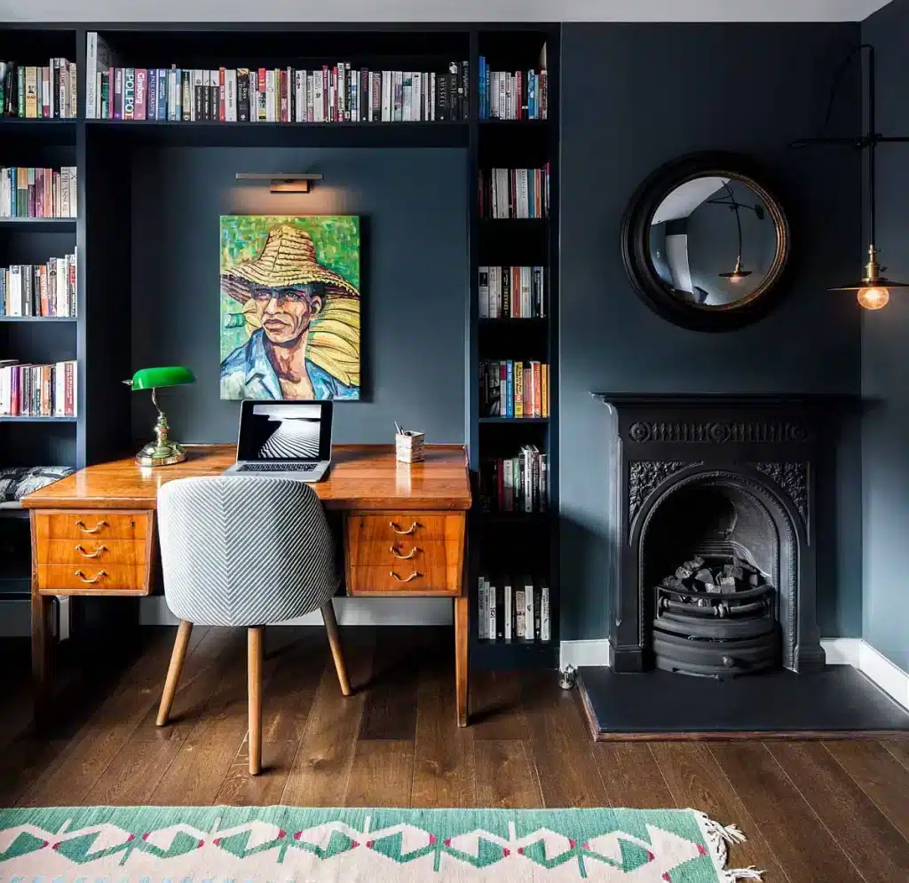 a vibrant art piece on black wall of a home office books stacked in shelves chair and wooden working desk