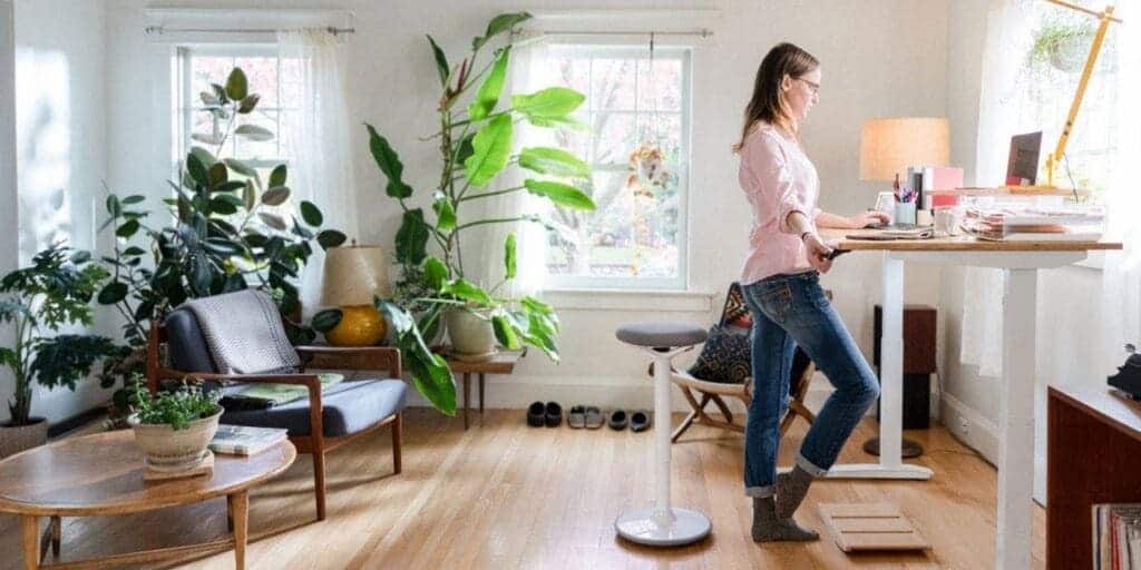 a woman stasnding near a desk working on laptop a lot of plants placed in the space