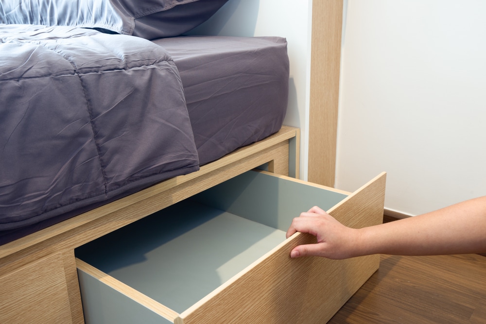 A human hand open the designed wooden drawer under the bed