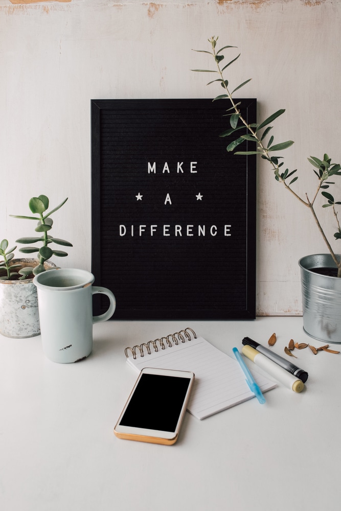 Cute styled workplace with inspirational text on black and white letter board, blank smartphone screen and notebook