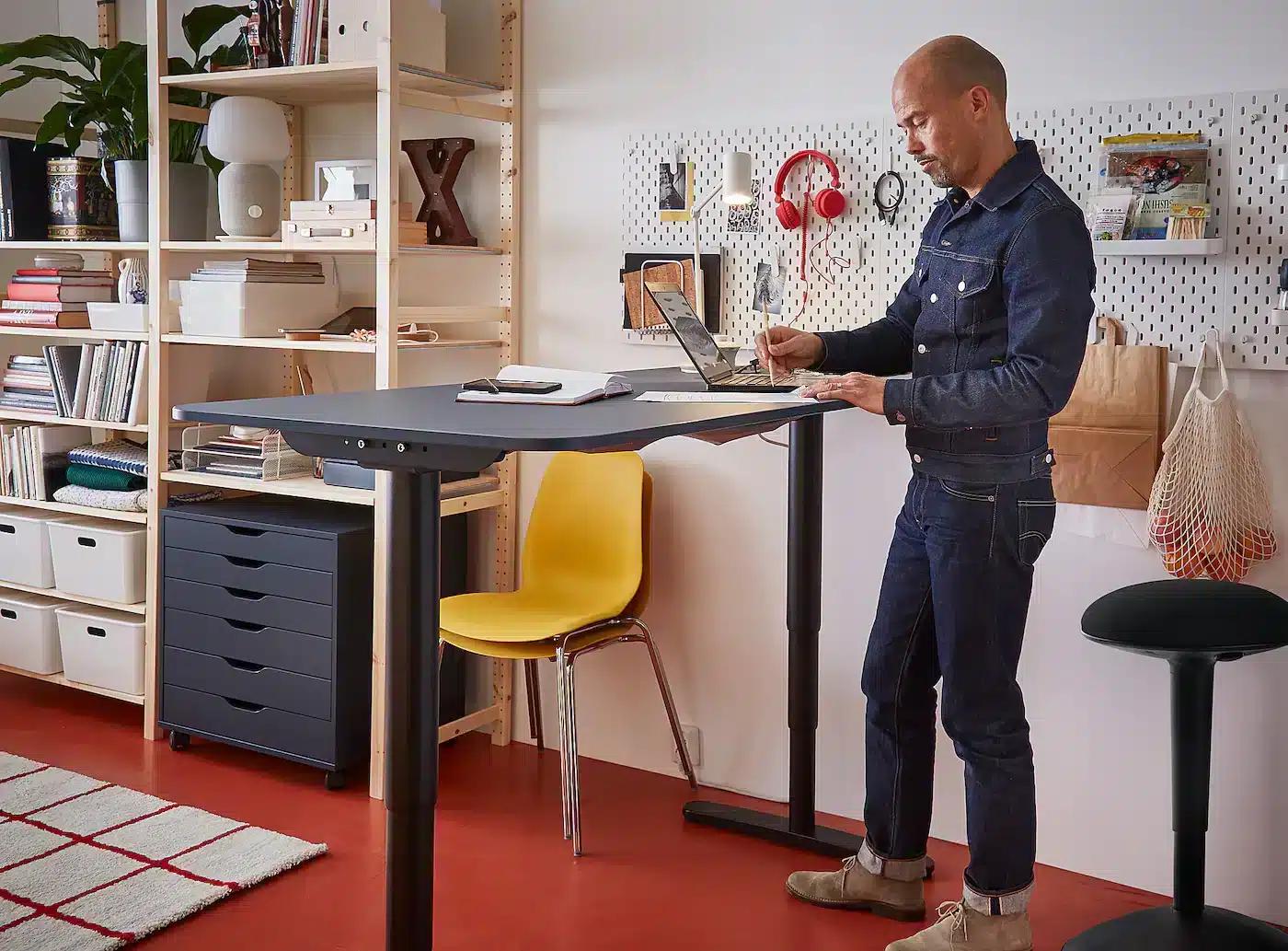 a person working on a laptop standing near a bekant desk books piled in shelves small chair