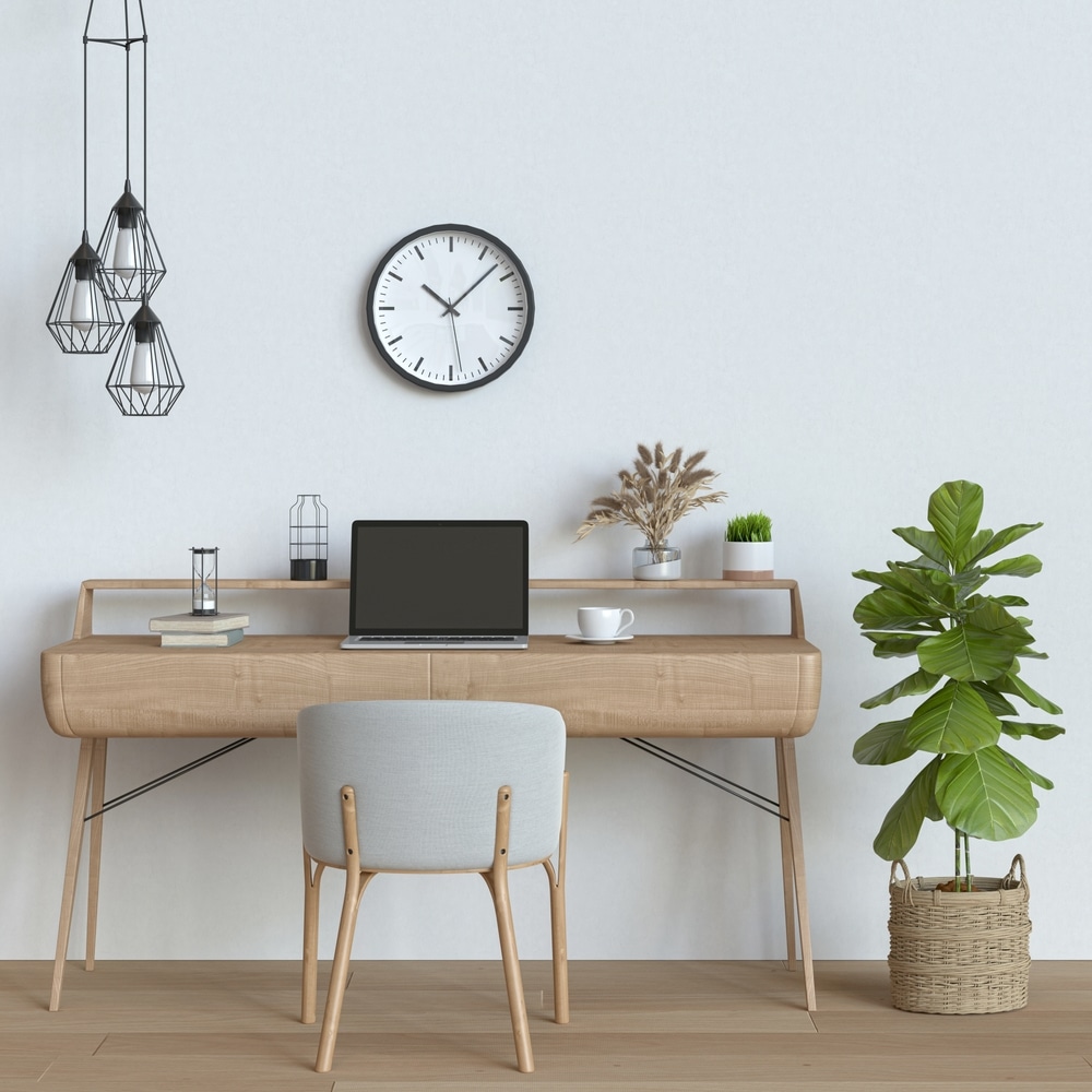 home office minimalist setup with clock on wall, hanging light fixtures, plant, laptop chair and a cup of tea on desk