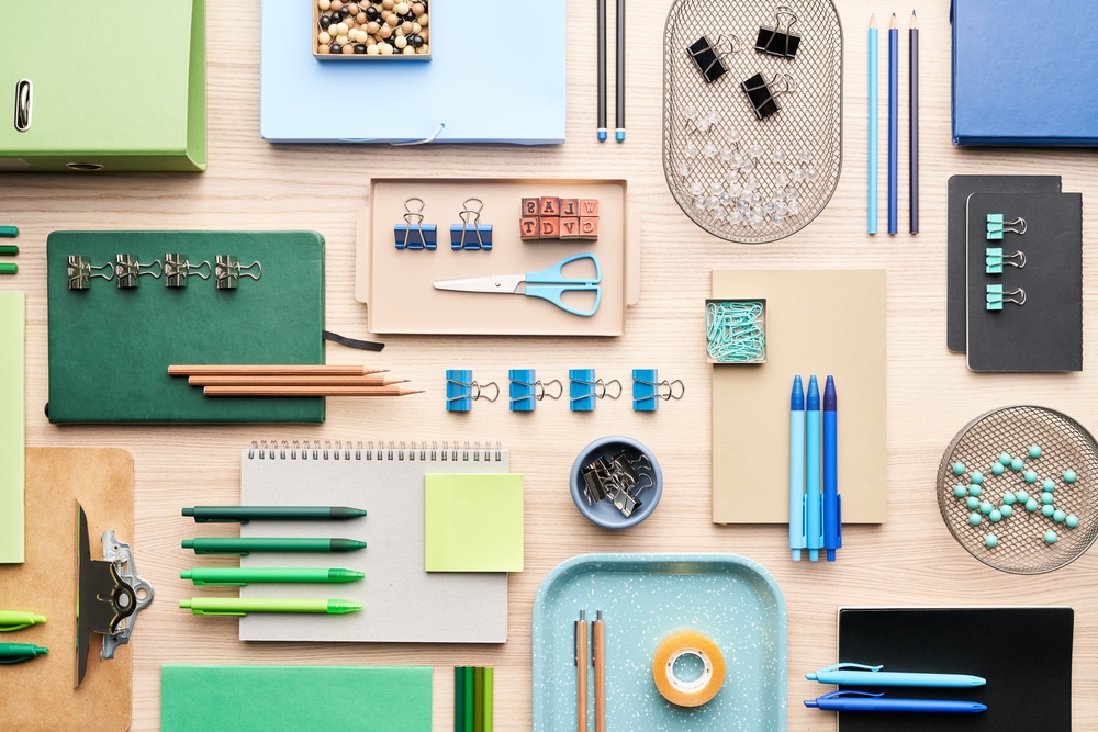 Flat lay of set of assorted modern stationery arranged in order on desk in office