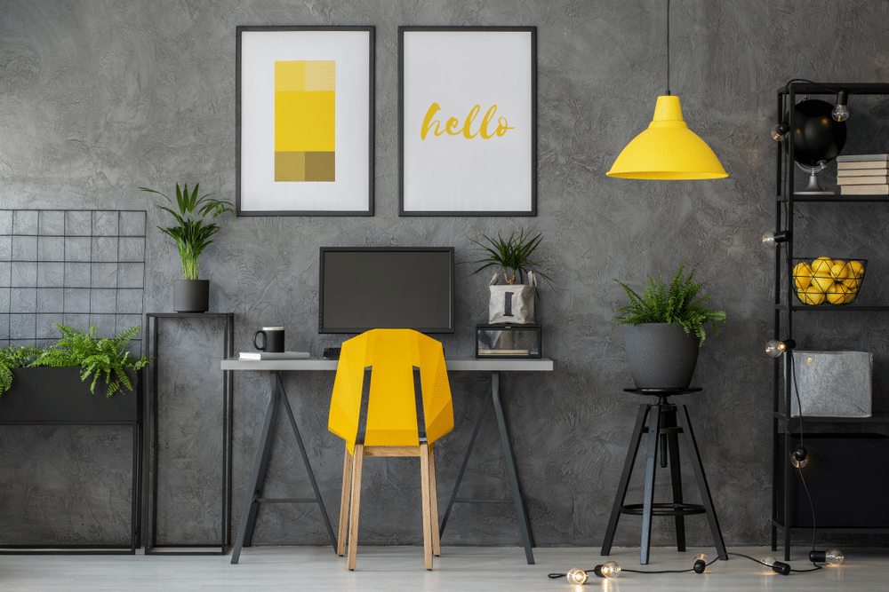 Stylish yellow and grey home office with industrial furniture and photo with posters on concrete wall