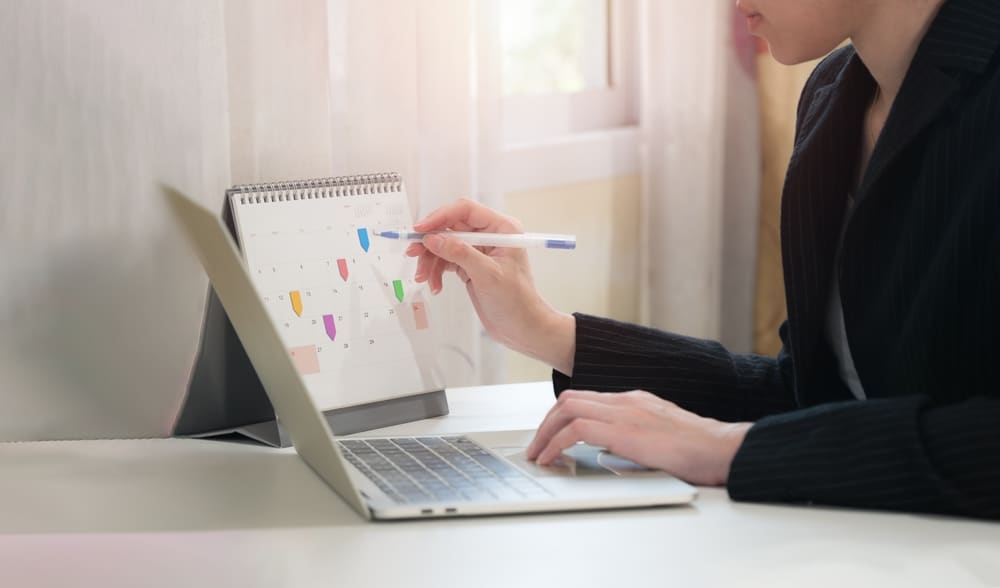 someone using phone to check planner and making notes on desk calendar