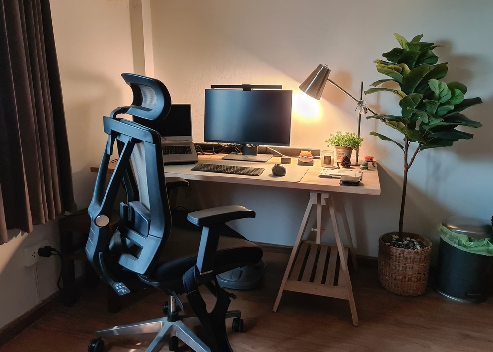 Working corner with monitor, laptop, wooden desk, ergonomic chair and plants in bedroom