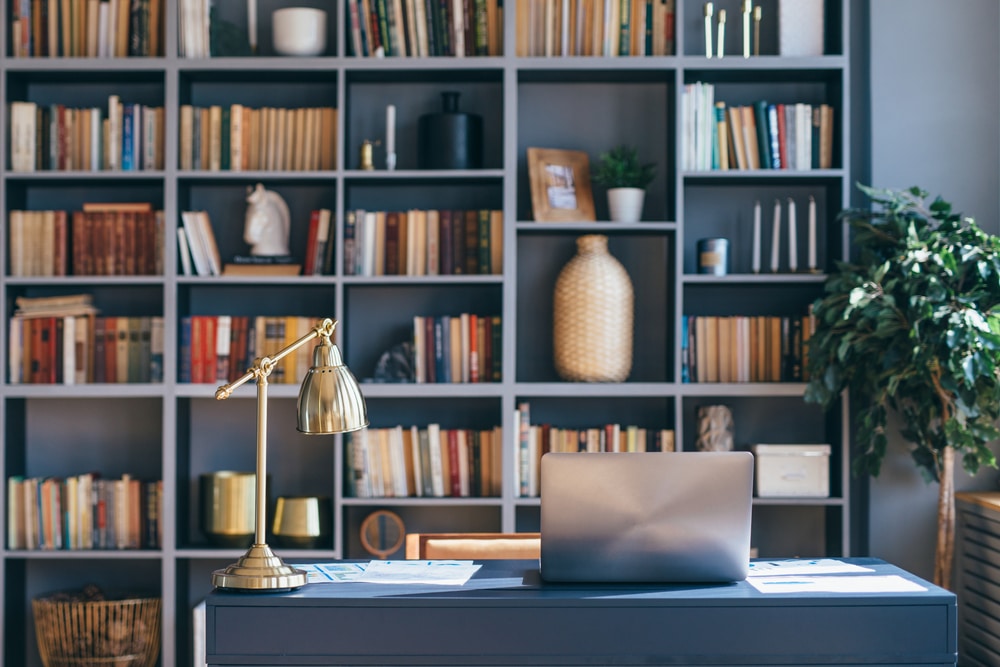 home office setup laptop and lamp on table near a book shelf