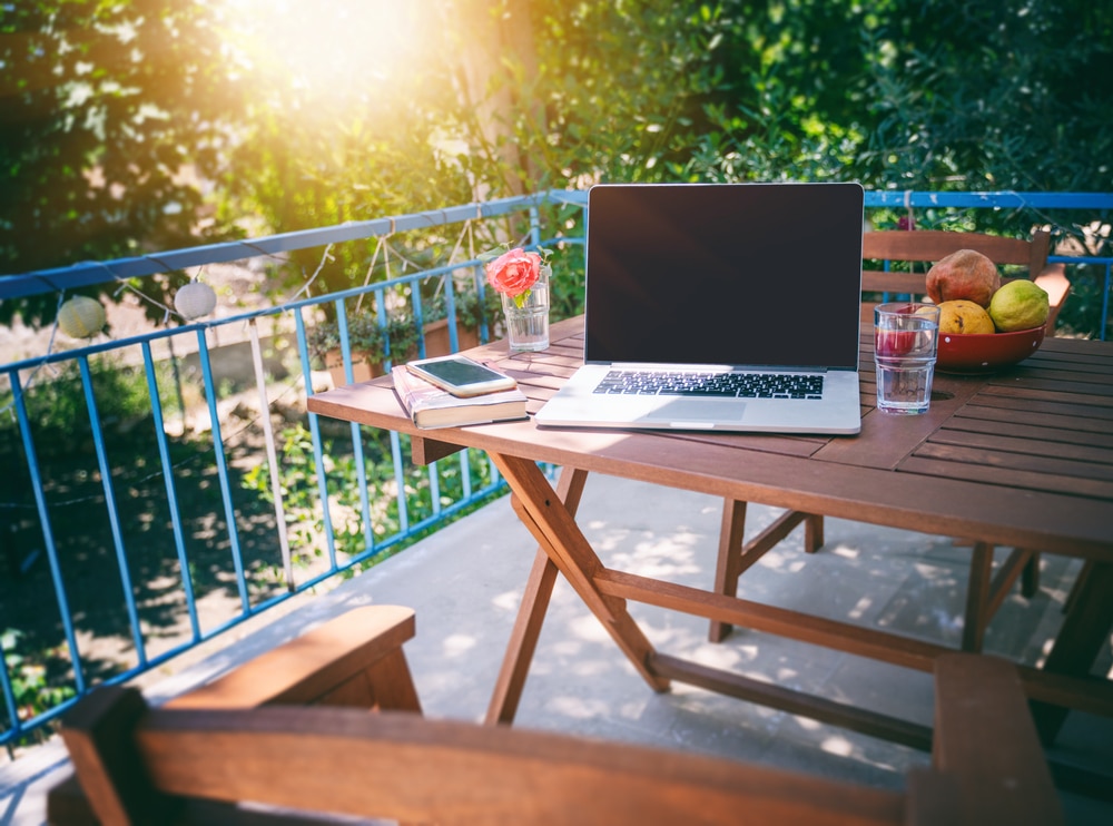 laptop phone and book placed on a wooden table in the balcony of house